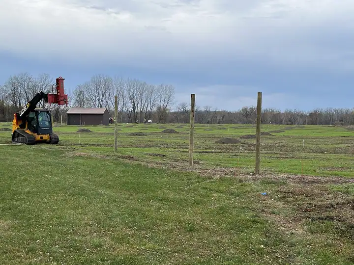Fence posts being set in a field with a tractor